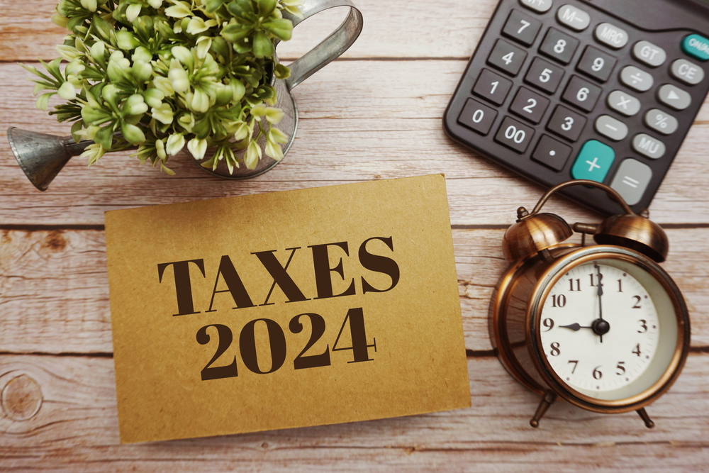 Paper reading Taxes 2024 on wood surface with clock, calculator, and plant