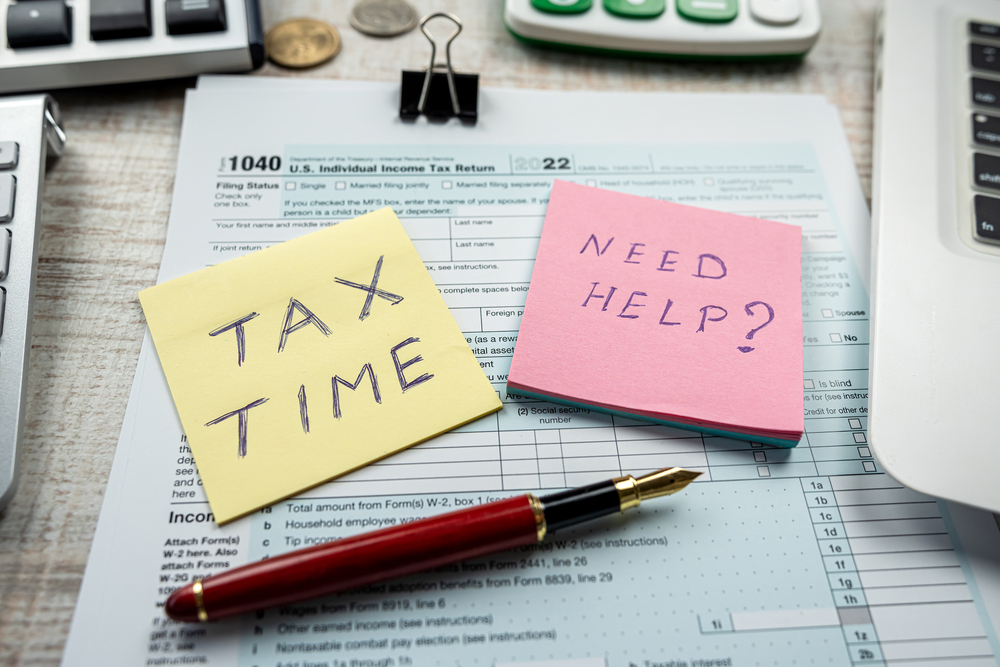 Sticky notes reading "tax time" and "need help?" next to laptop, tax papers, and pen