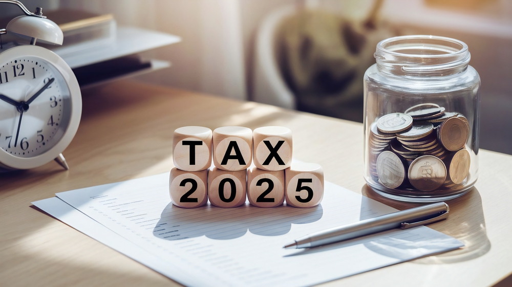 Blocks spelling Tax 2025 on desk with papers, clock, pen, and jar of coins