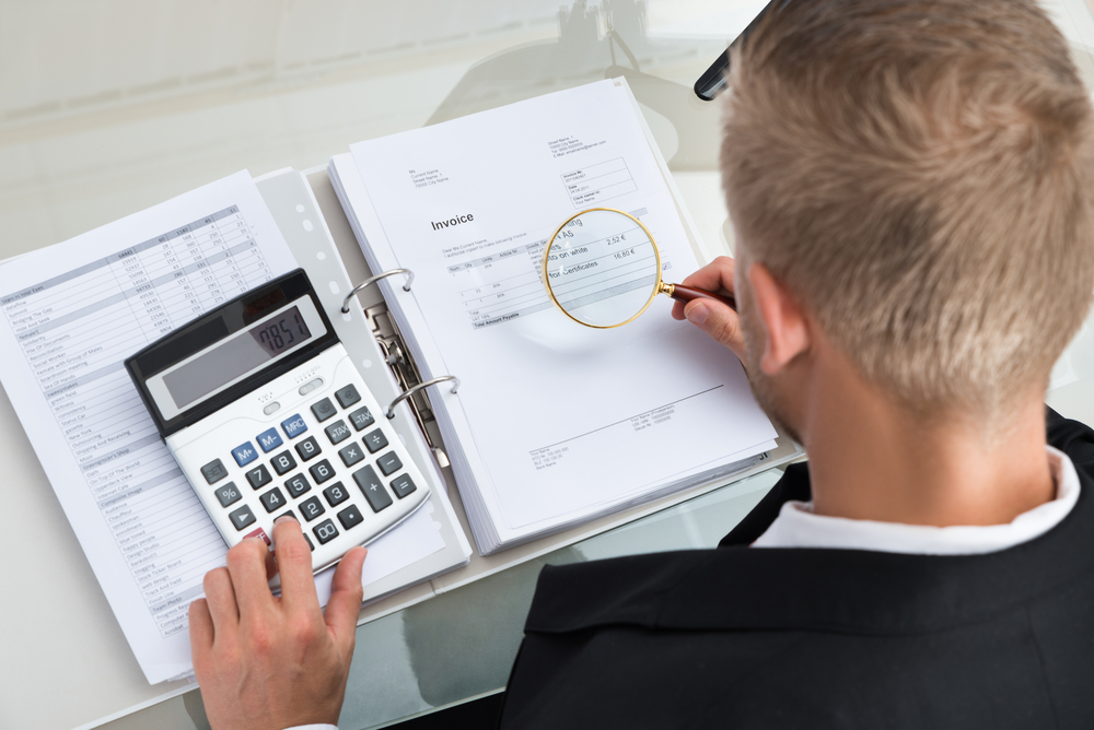 Businessman going through documents with magnifying glass and calculator