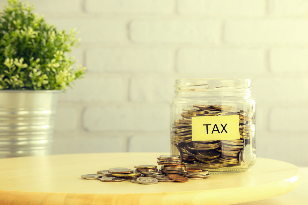 "Tax" label on jar full of coins with some coins spilled on counter