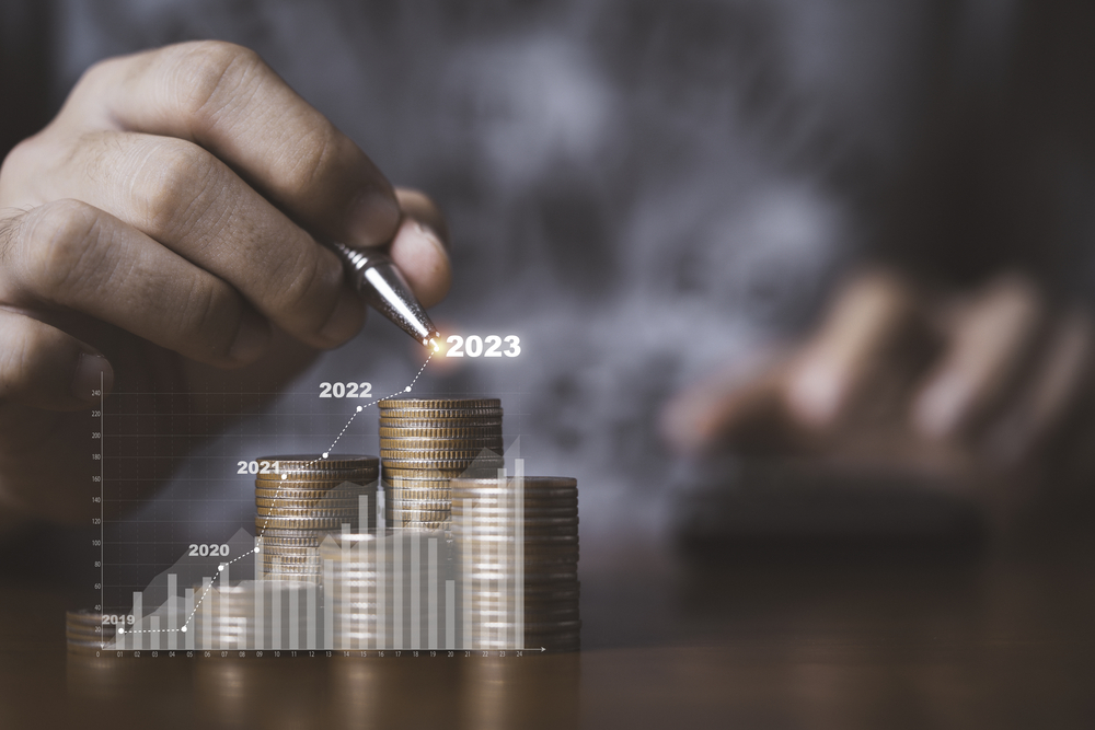 Hand with pen counting stacks of coins, overlaid with graph showing increasing profits