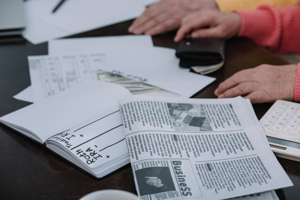 Couple with money, newspaper, and notebook comparing traditional and Roth IRA