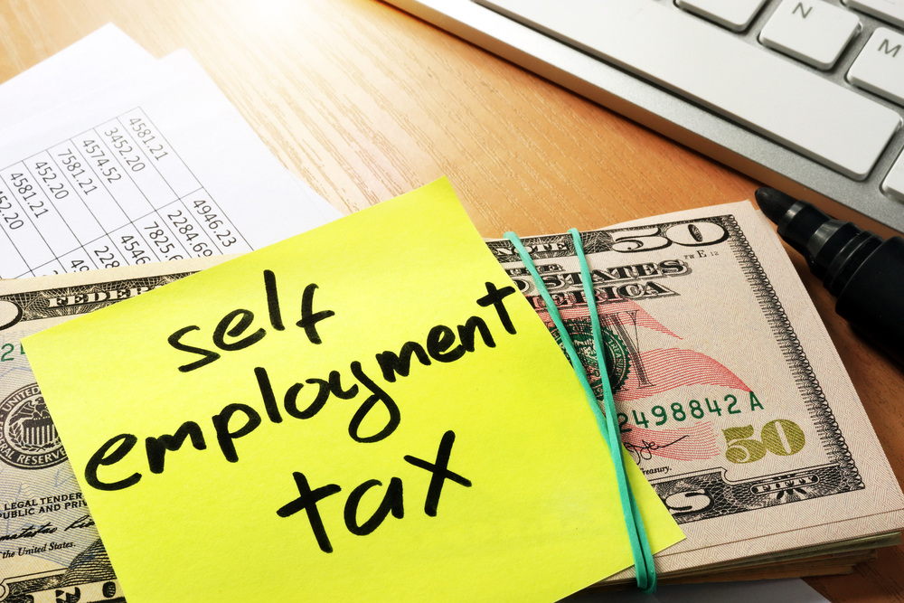 Stack of money with sticky note labeled self employment tax