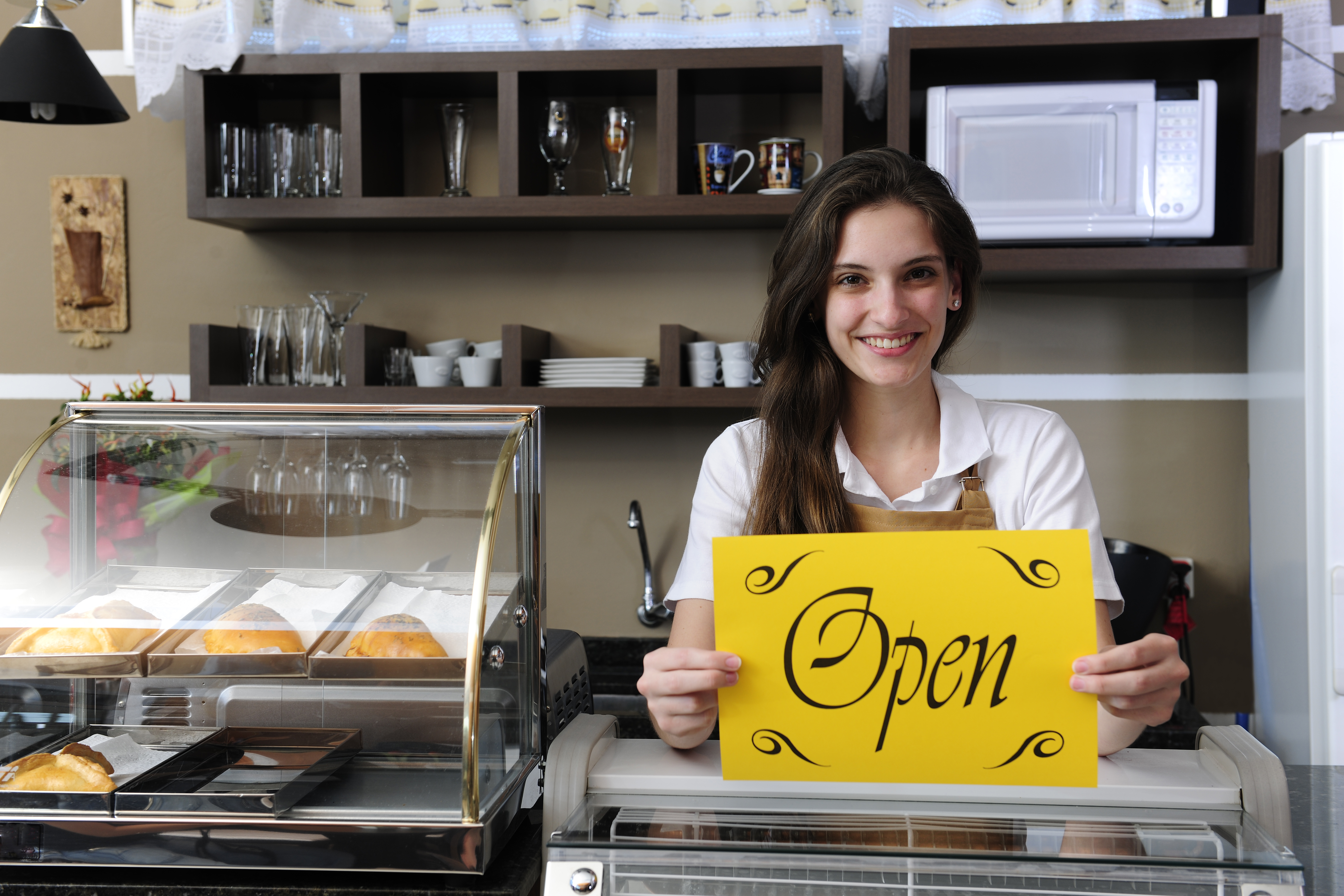 Woman behind cafe counter holding Open sign