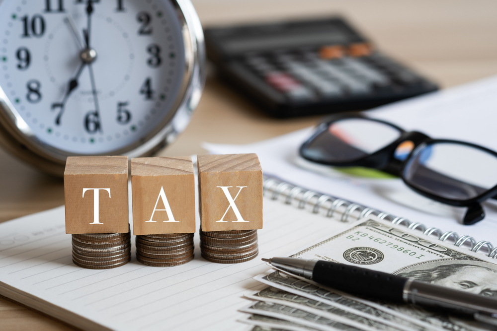 TAX spelled out on wood blocks with coins, cash, and calculator nearby