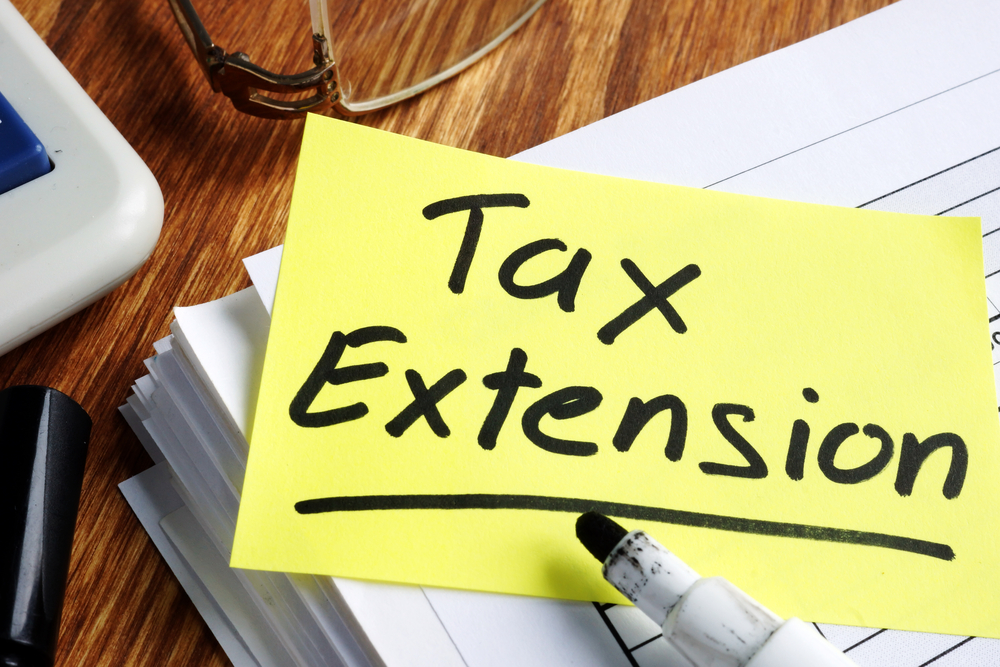 Tax extension written on yellow sticky note on top of tax documents