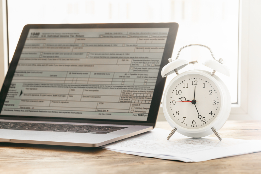 Form 1040 on laptop screen next to alarm clock